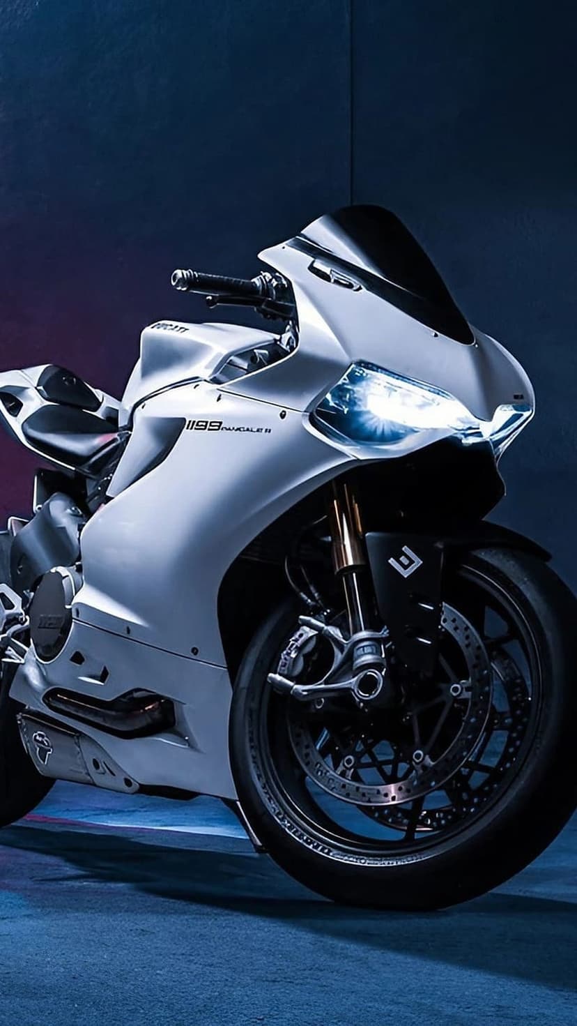 White Ducati 1199 Panigale R motorcycle with glowing headlights against a dark, low-angle background.