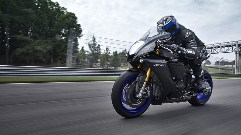 Black Yamaha R1M motorcycle with blue wheels racing on a track with motion blur and green background trees.