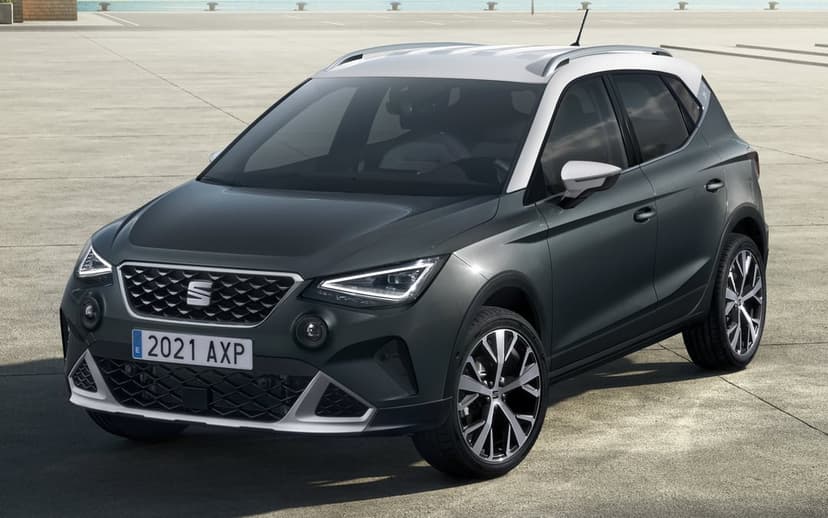 Dark grey SEAT Arona SUV with a white roof parked on a sunny concrete waterfront with distant blue water.