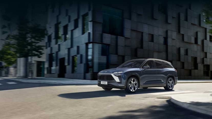 Dark grey electric SUV driving on a city street next to a modular black building with soft shadows.