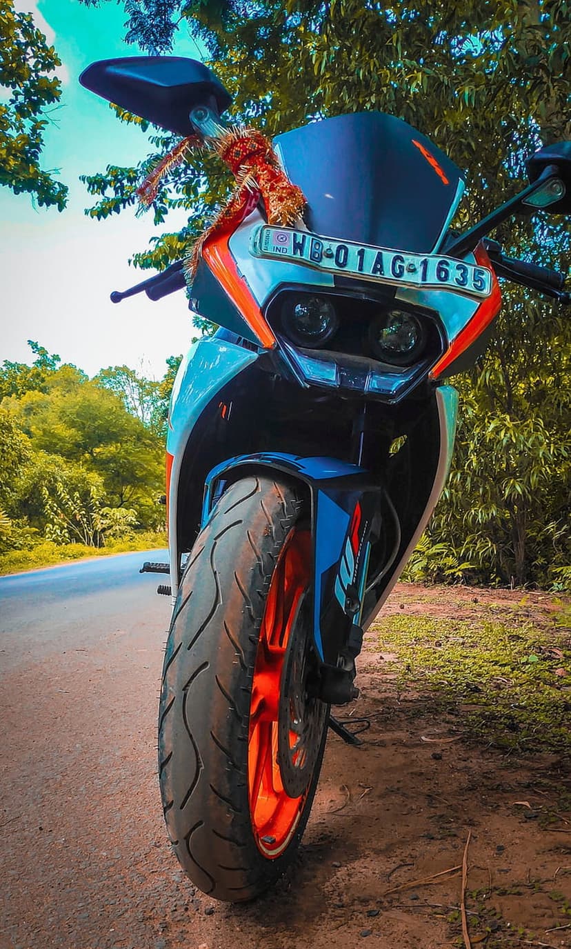 KTM RC motorcycle with orange and blue accents parked on a dusty forest road surrounded by green trees.