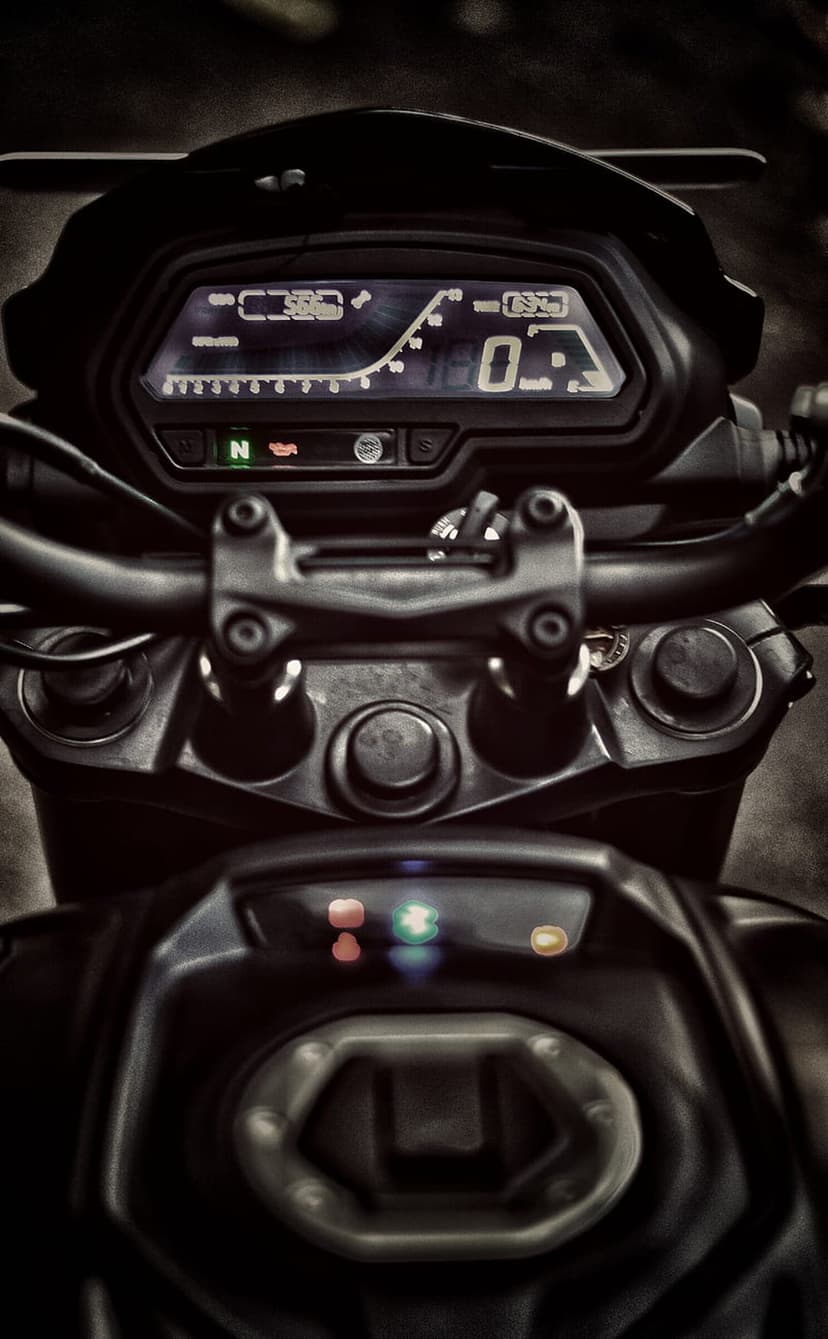 Digital motorcycle dashboard displaying a speedometer, gear indicator, and lit warning icons on a dark display.