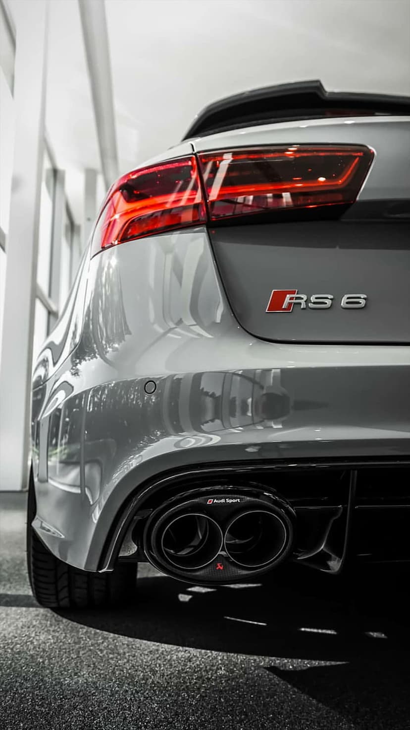 Audi RS 6 rear view featuring silver metallic paint, glowing LED taillights, and black quad exhaust outlets.