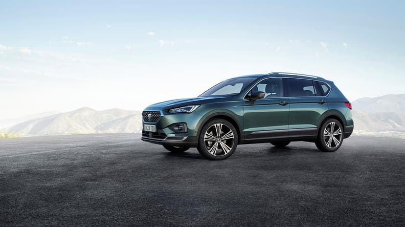 Dark green SEAT Tarraco SUV parked on asphalt with a hazy mountain range and clear sky in the distance.