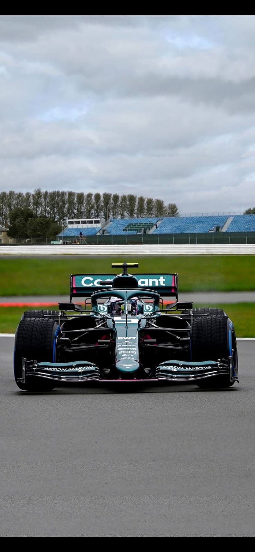 Aston Martin F1 car in British racing green drives on an asphalt track under a cloudy, overcast sky.