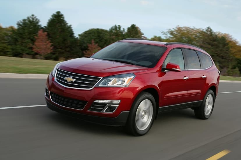 Red Chevrolet Traverse SUV driving on a road with green trees and a soft blue sky in the background.