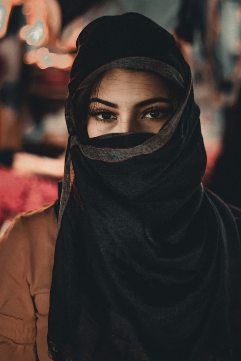 Woman with captivating eyes wears a black hijab that partially covers her face against a blurred background.