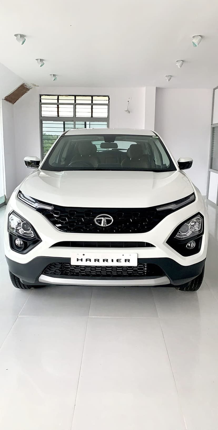 White Tata Harrier SUV with LED headlights parked on a reflective tile floor inside a modern vehicle showroom.