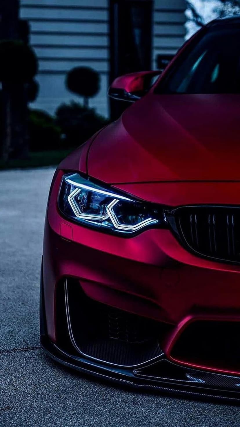 Sharp LED headlight of a crimson sports car glows against a matte red fender in a close-up night view.