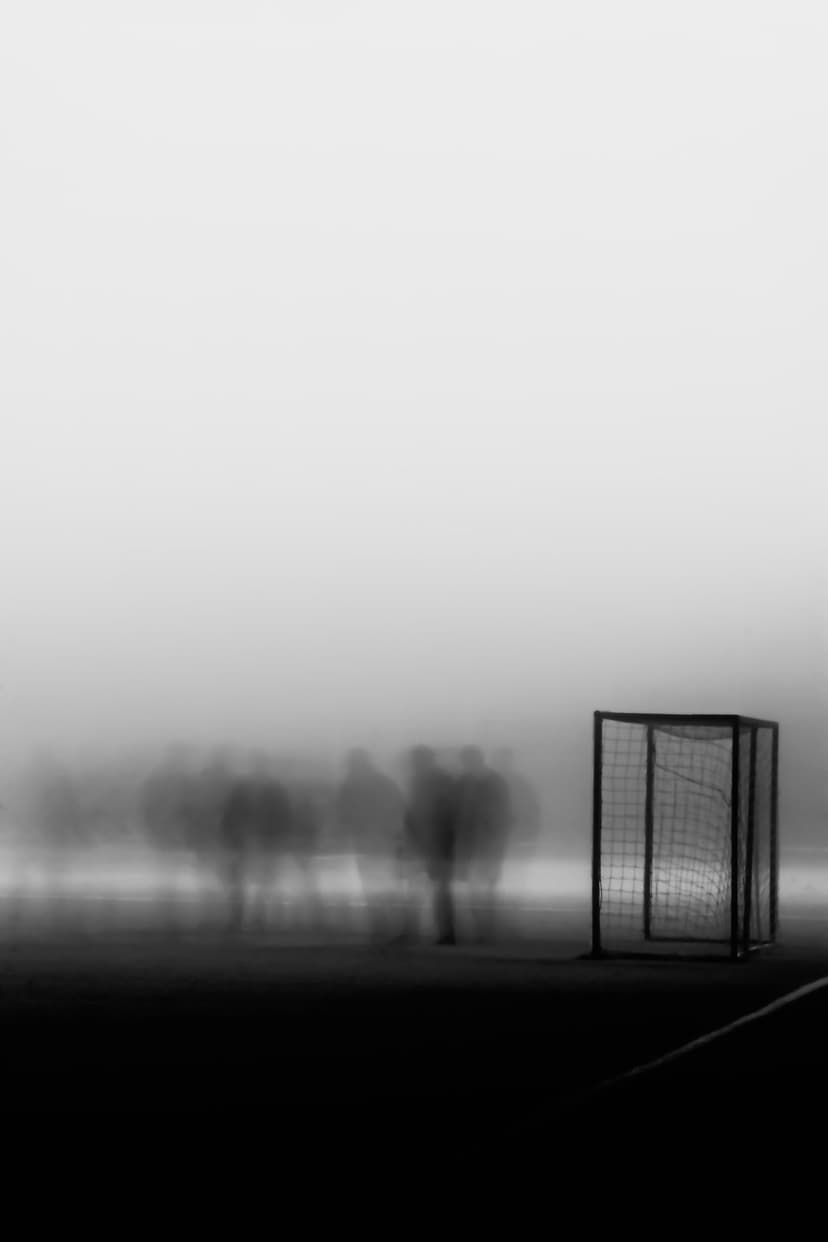 Soccer goal on a misty beach with blurred silhouettes of people walking in the distance under a foggy sky.