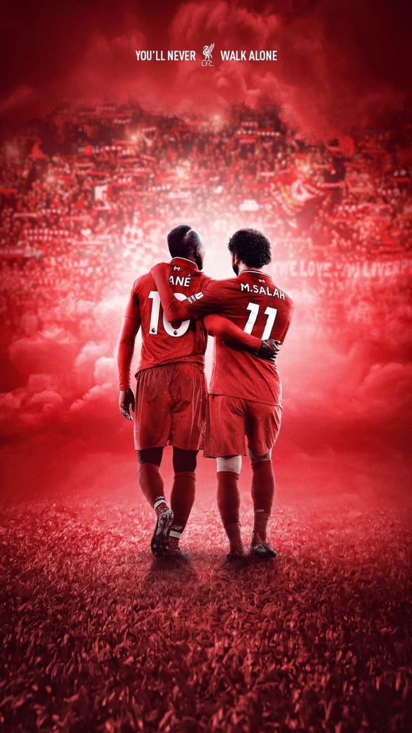 Sadio Mane and Mohamed Salah stand arm-in-arm facing a crowd with You'll Never Walk Alone text in a red stadium.