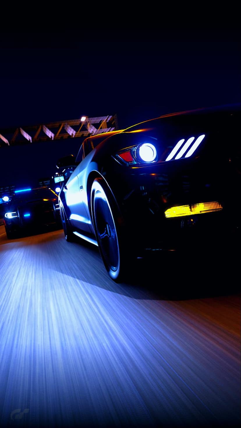 Black Ford Mustang with glowing headlights leads a police chase under a dark highway overpass at night.