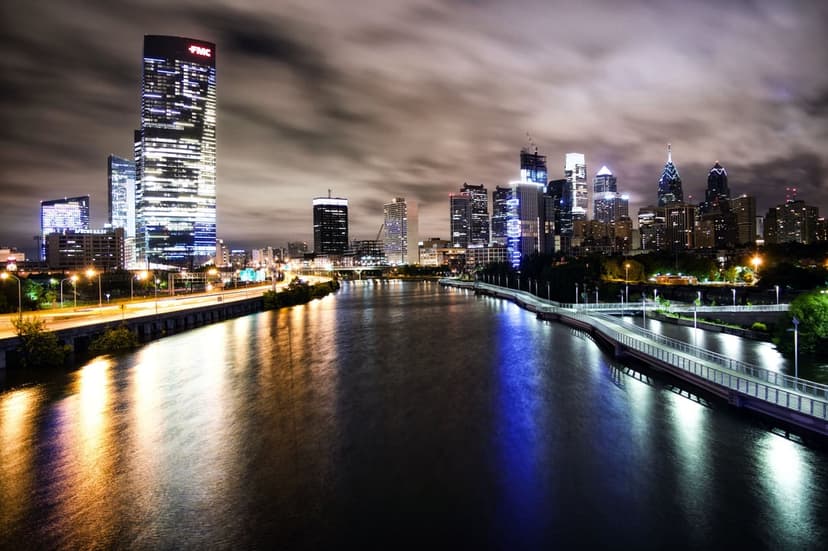 Philadelphia skyscrapers with glowing windows reflecting on the Schuylkill River under a cloudy night sky.
