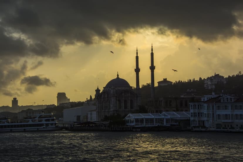 Silhouette of a mosque with two minarets against a golden sunset sky and a ferry boat on the Bosphorus water.