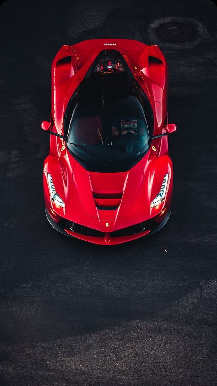 Red Ferrari supercar with a black roof parked on dark asphalt, shown from a direct overhead bird's-eye view.