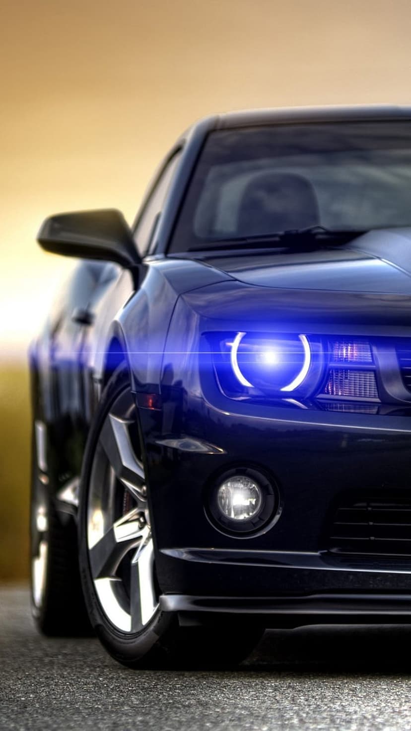 Dark blue sports car featuring glowing neon LED headlights and an aggressive front bumper in vertical view.