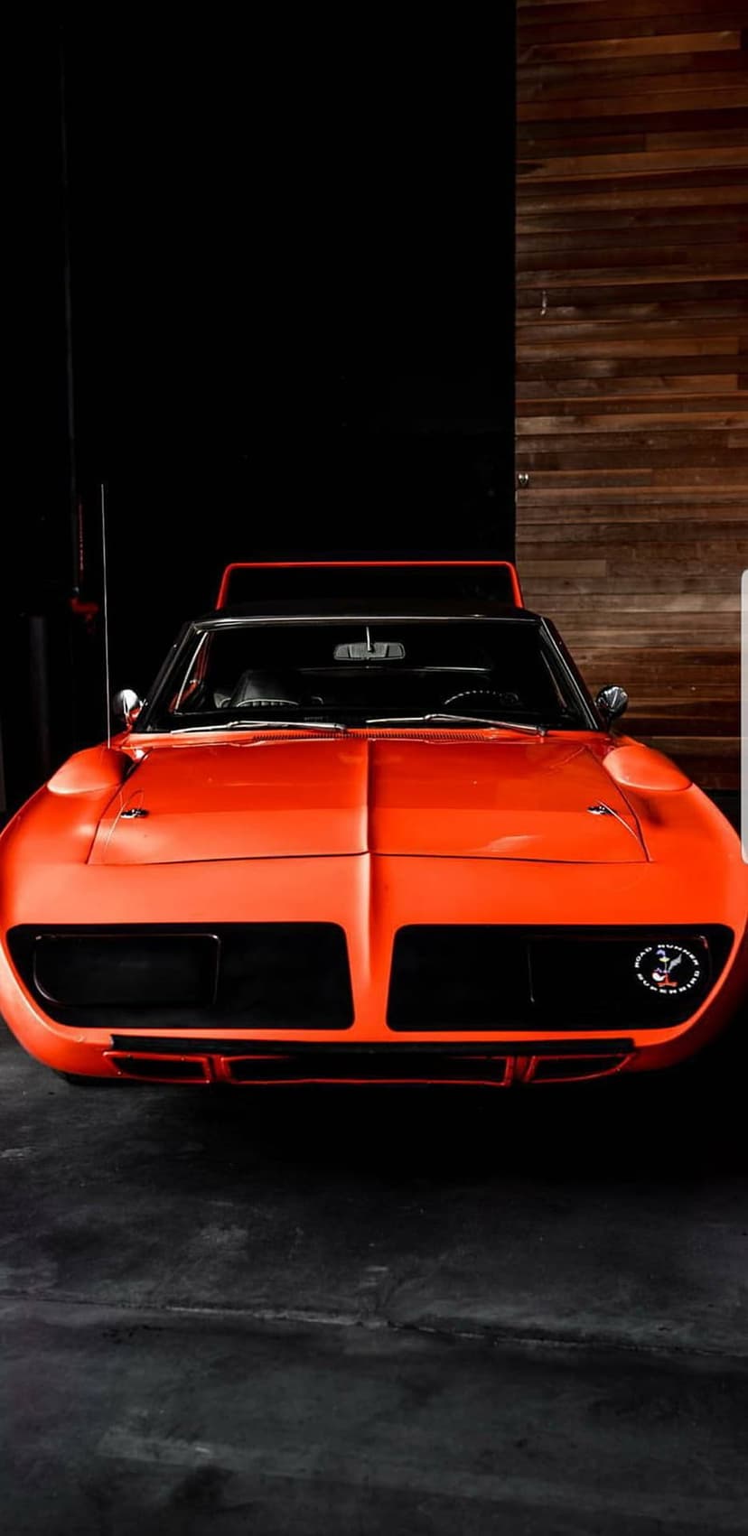 Orange 1970 Plymouth Superbird featuring a pointed nose cone stands before a dark, textured wood background.