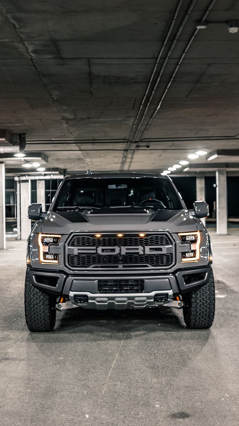 Front view of a grey Ford F-150 Raptor with glowing amber lights in a dark, concrete underground parking garage.