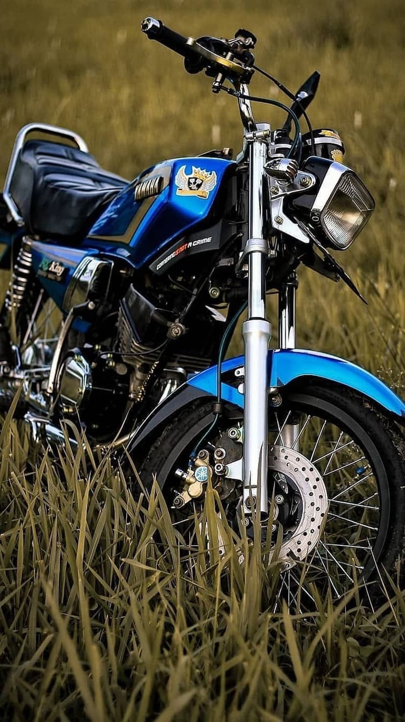 Blue Yamaha RX King motorcycle with chrome handlebars and round headlight parked in a field of tall dry grass.