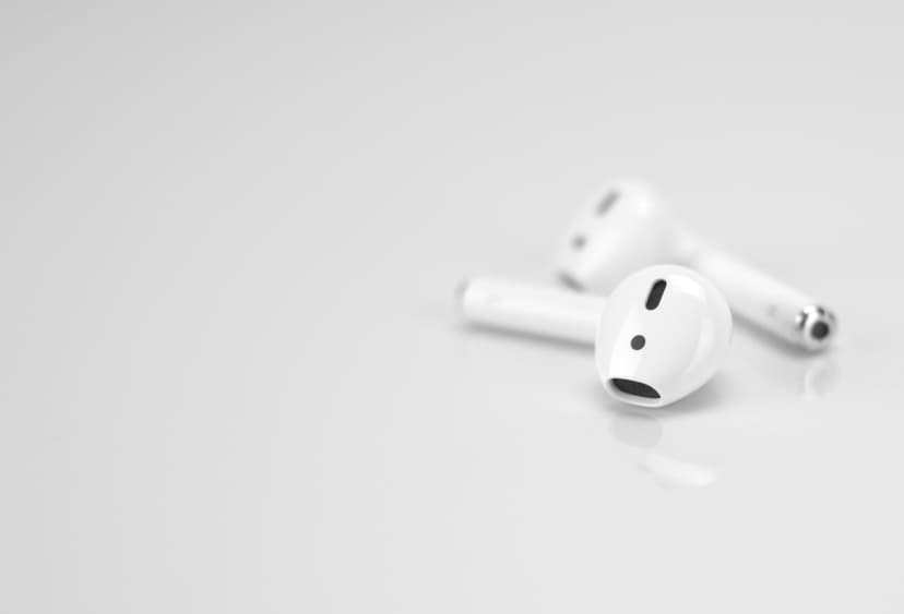 Two white wireless earbuds rest on a reflective surface showcasing their smooth curves and tiny speaker grilles.
