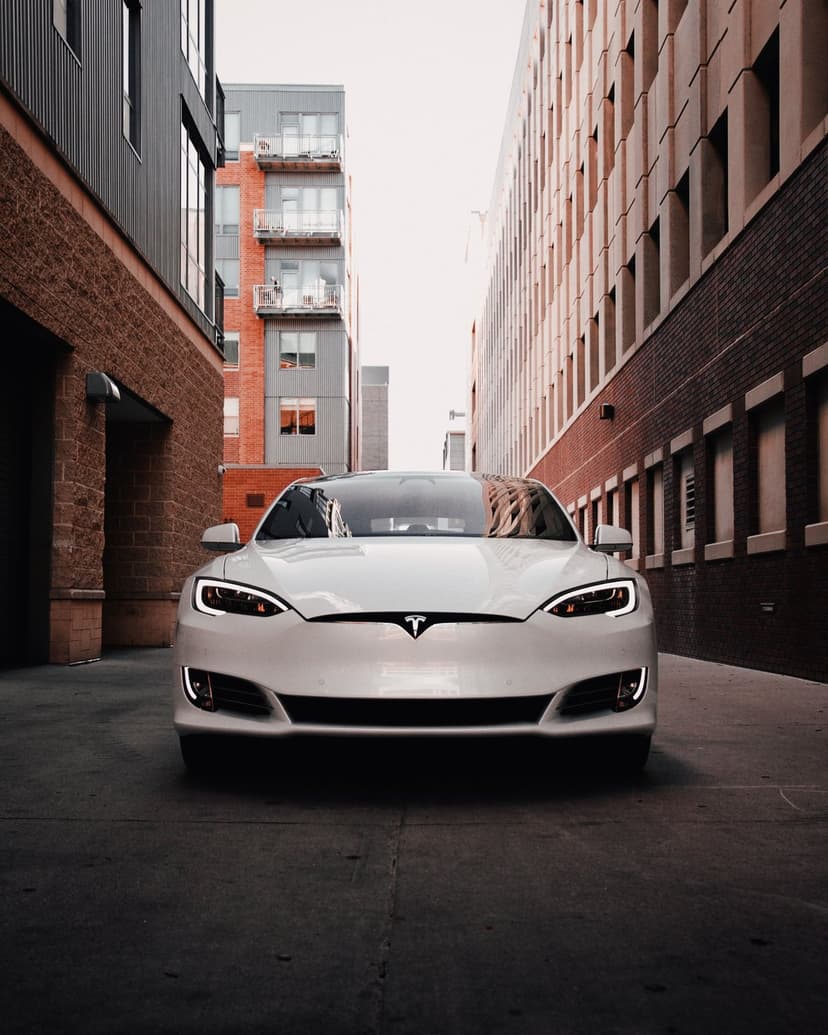 White Tesla electric sedan parked in a narrow alley between brick and glass buildings under soft city light.