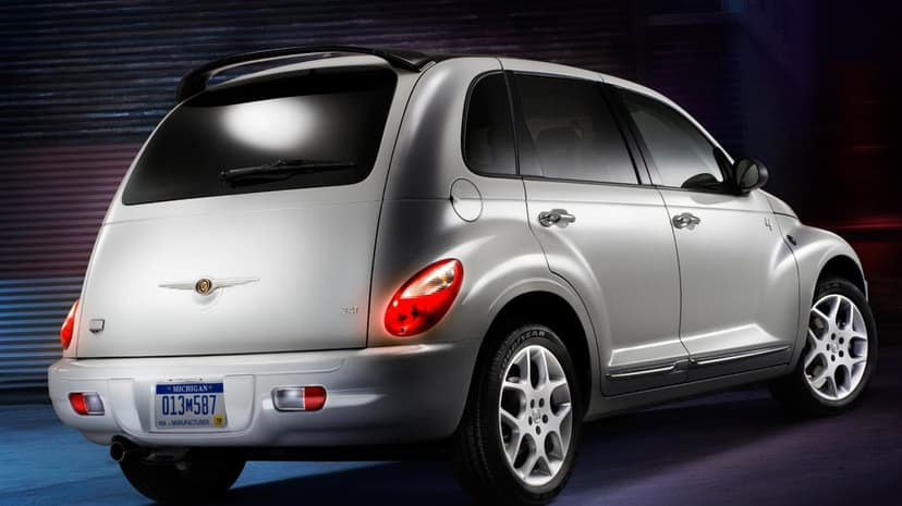 Silver Chrysler PT Cruiser with a rear spoiler and glowing taillights set against a dark garage background.