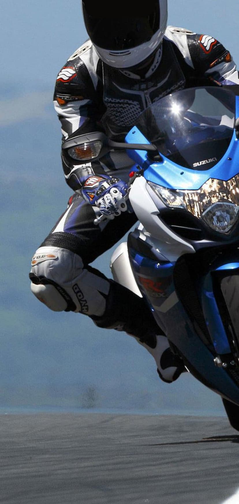 Motorcyclist in blue and white racing leathers leans a sportbike into a sharp turn on a blurred asphalt track.