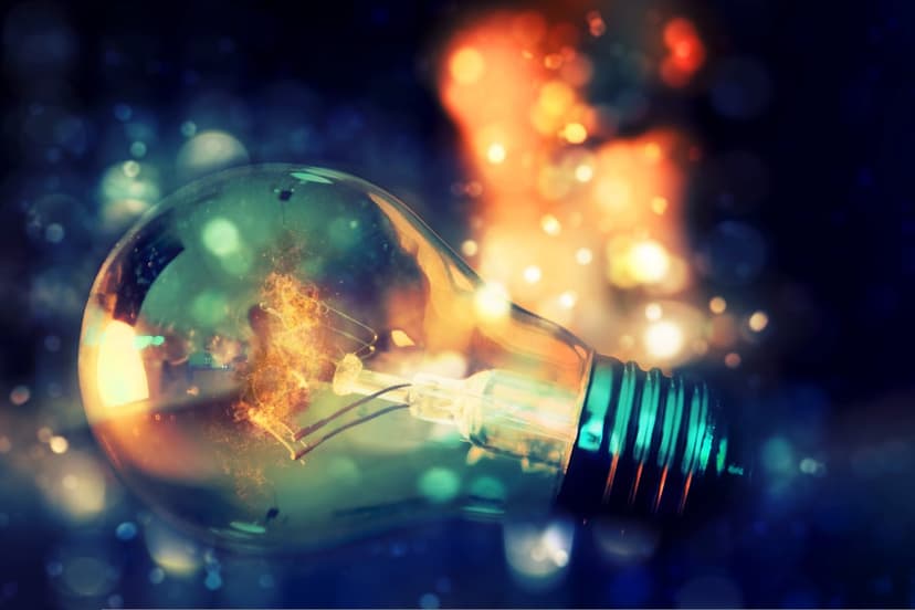 Clear light bulb filled with swirling orange energy lying on its side amidst blue and gold bokeh light orbs.