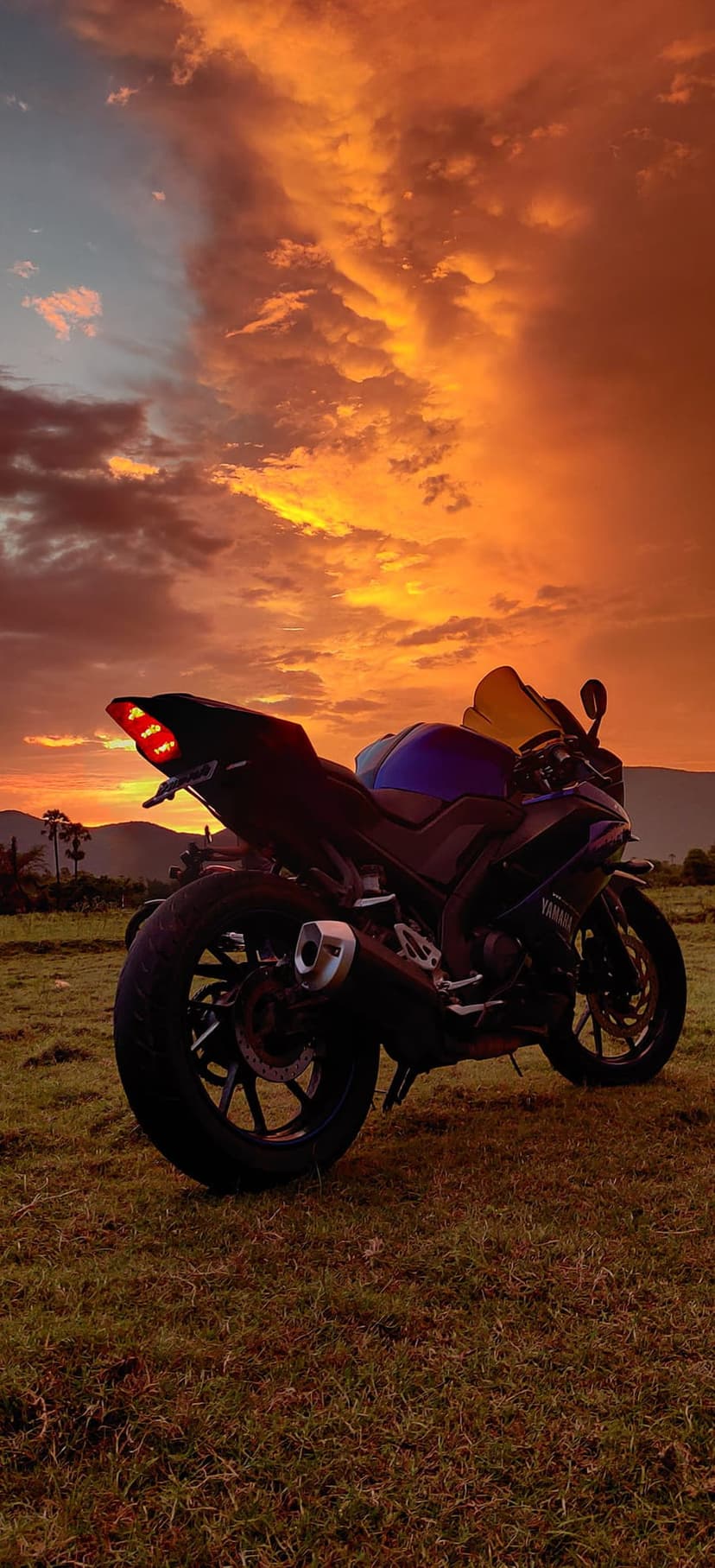 Sportbike silhouette with glowing red brake lights against an orange sunset sky and a grassy field at dusk.