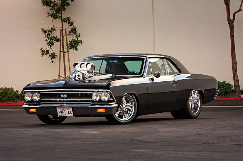 Black 1966 Chevrolet Chevelle SS with a chrome blower on the hood parked on asphalt under soft light.