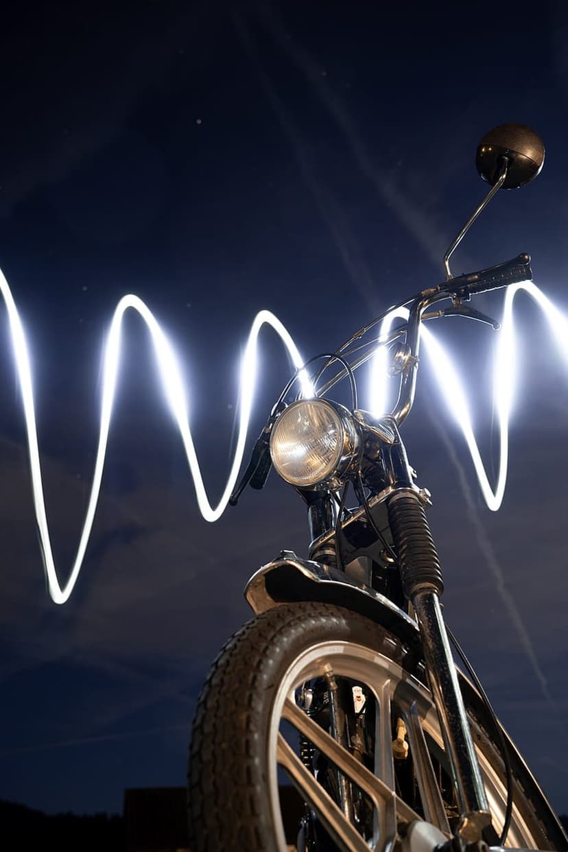 Vintage motorcycle with chrome details parked under a wavy neon light trail against a dark night sky background.