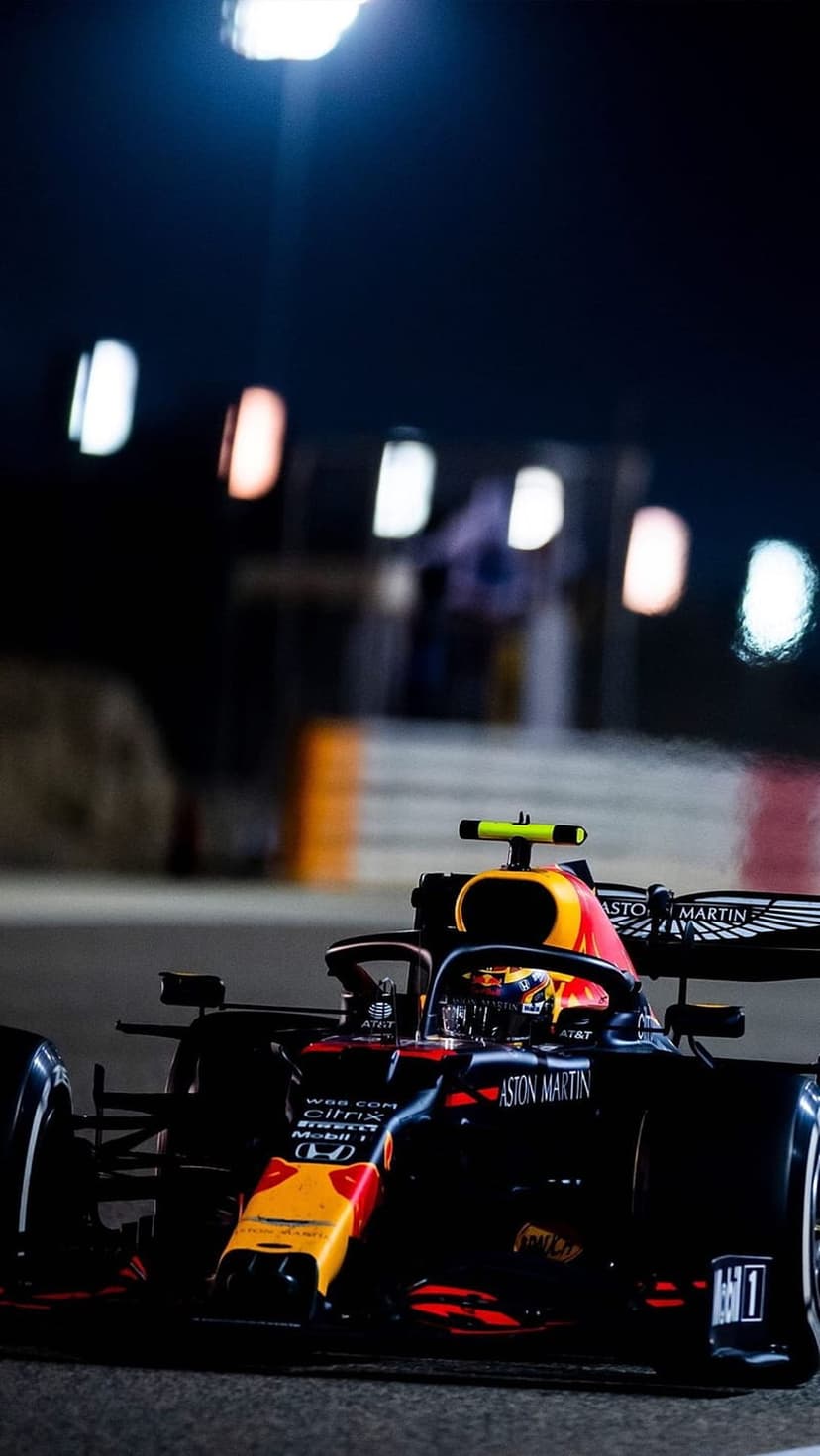Red Bull Racing F1 car with matte navy and yellow livery speeds past glowing track lights during a night race.
