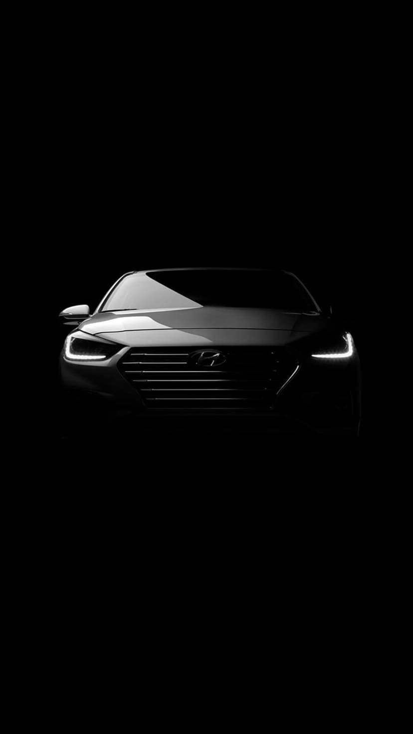 Hyundai car headlights and textured front grille illuminated against a dark black background in monochrome.