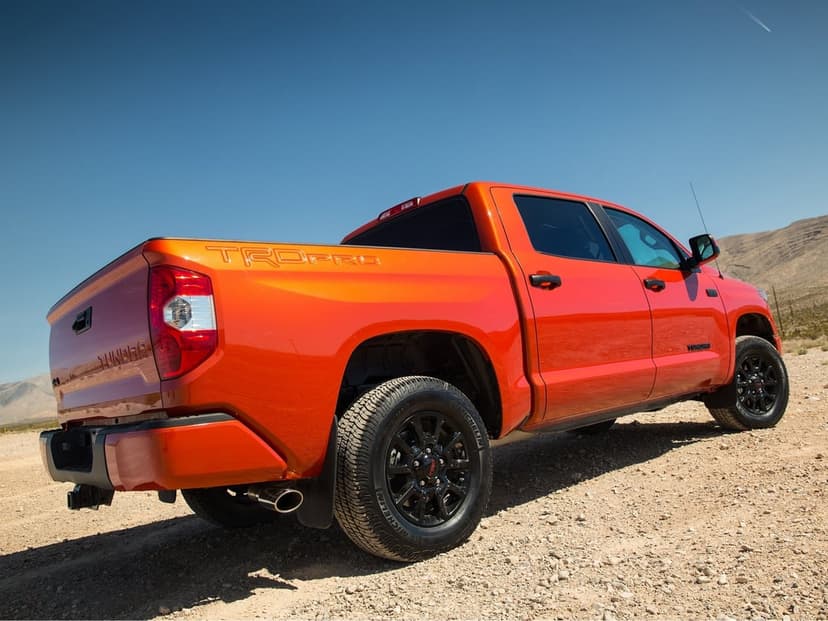 Orange Toyota Tundra TRD Pro truck with black wheels parked on a gravel road under a clear blue desert sky.