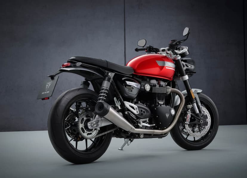 Red Triumph Speed Twin motorcycle parked against a dark grey wall in a studio with soft side lighting.