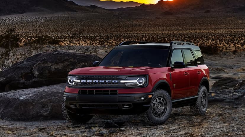 Red Ford Bronco Sport SUV parked on rocky desert ground with mountains under a golden sunset sky.