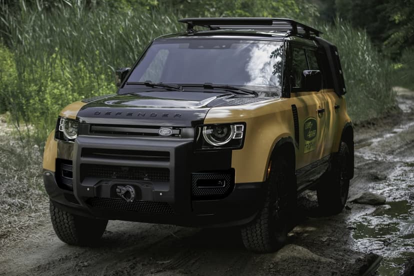 Land Rover Defender Trophy Edition on a muddy forest trail with a black hood, yellow body, and roof rack.