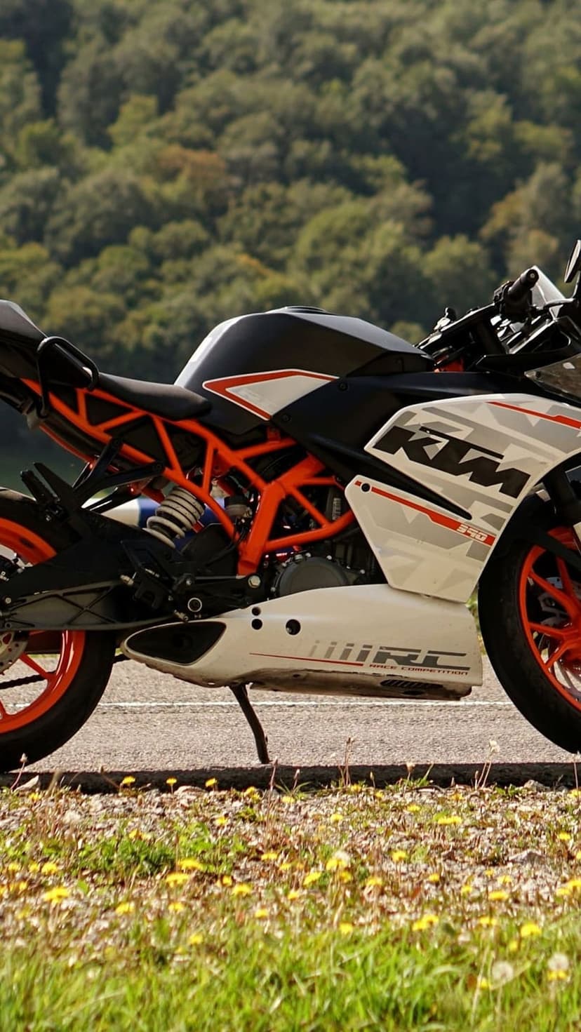 KTM RC 390 sportbike with an orange trellis frame parked beside a grassy field filled with yellow wildflowers.