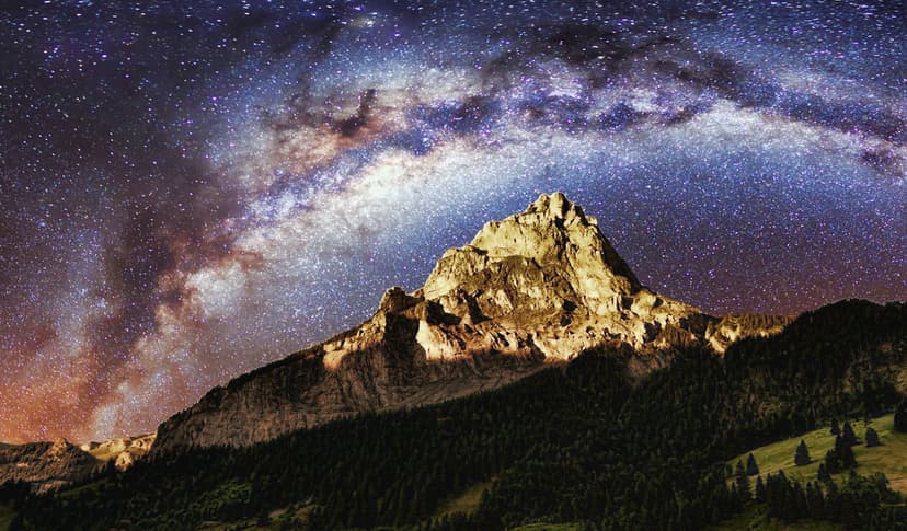 Rugged mountain peak stands under a glowing purple Milky Way galaxy and dense fields of distant white stars.