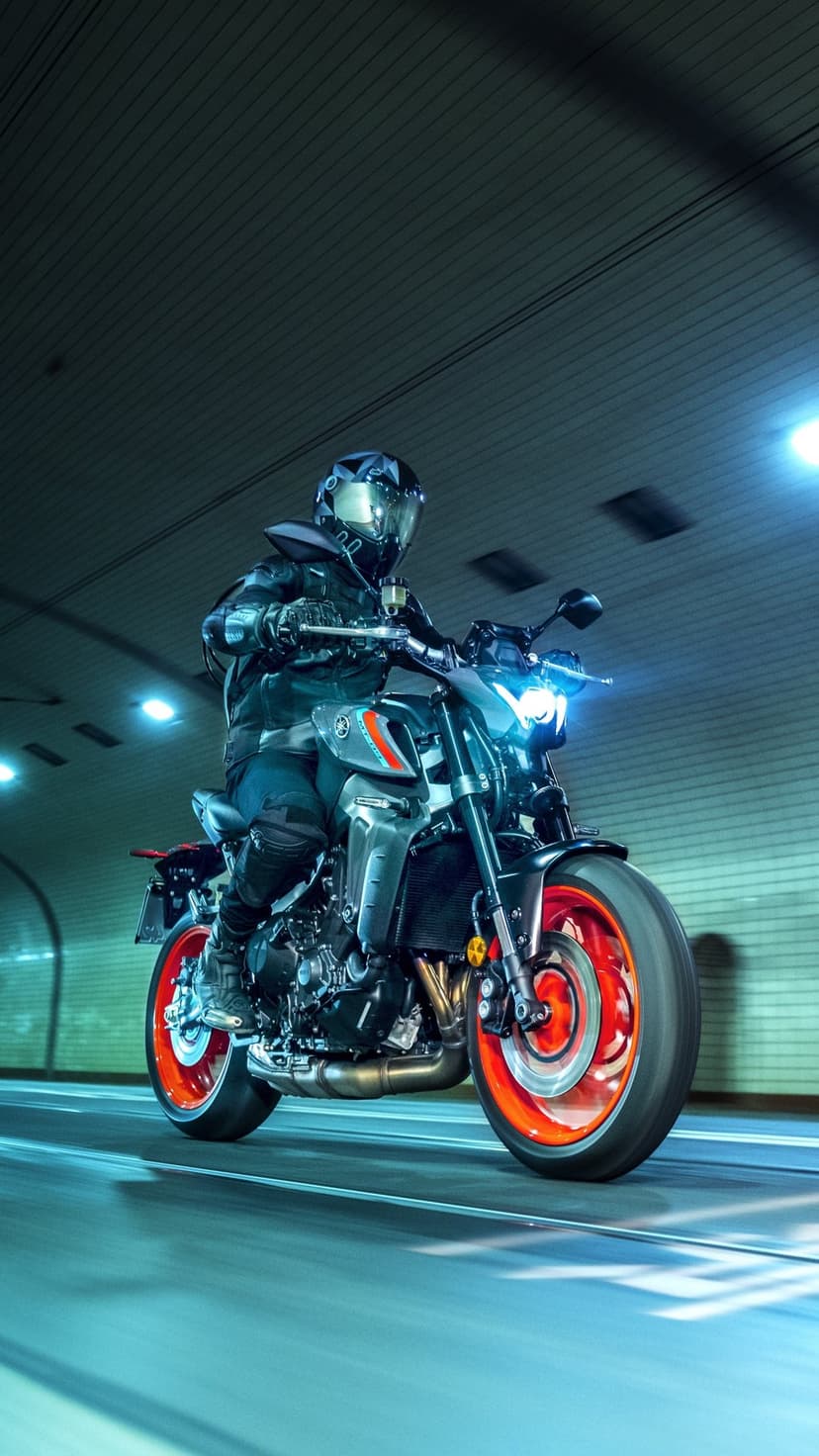 Motorcyclist in dark gear riding a gray Yamaha MT-09 with bright orange wheels through a blue-lit tunnel.