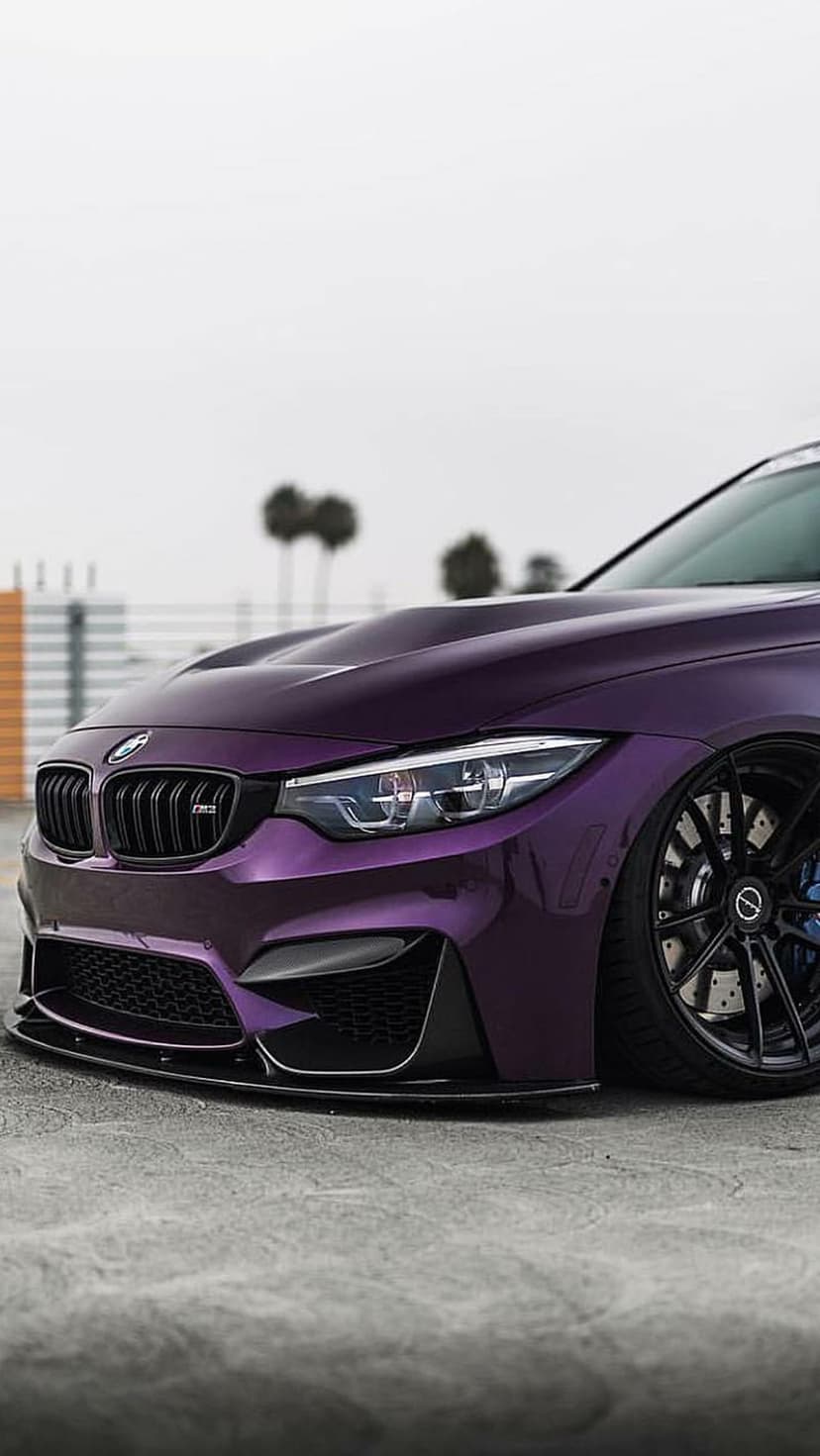 Purple BMW M4 sports car with black rims, blue calipers, and dark grilles parked on asphalt near palm trees.