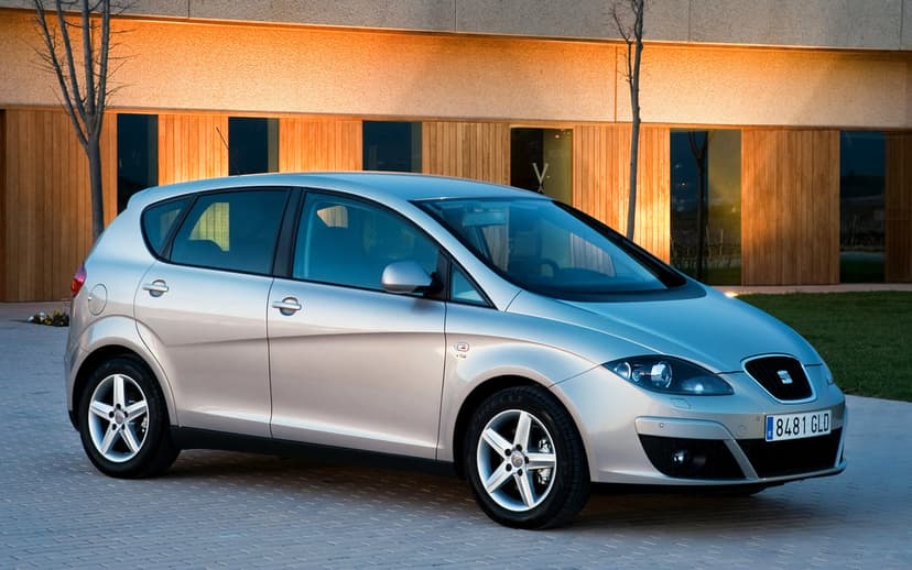 Silver SEAT Altea hatchback parked in front of a modern wood-paneled building during golden hour.
