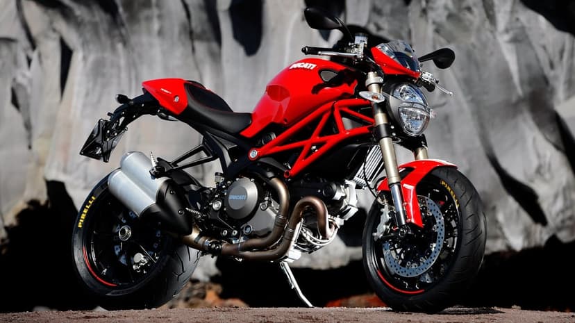 Red Ducati Monster motorcycle with a trellis frame parked in front of a gray rocky cliffside.