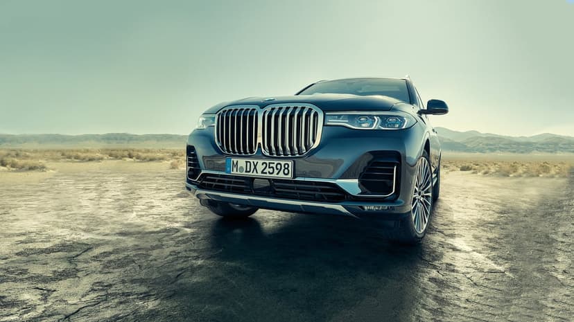 Dark blue BMW X7 luxury SUV front view on a cracked desert salt flat with mountains and a teal sky background.