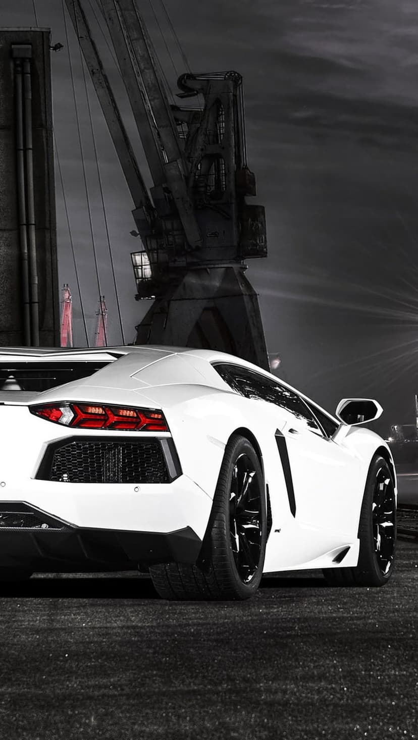 White Lamborghini Aventador parked at a dark industrial dock next to a large crane under cinematic night lighting.