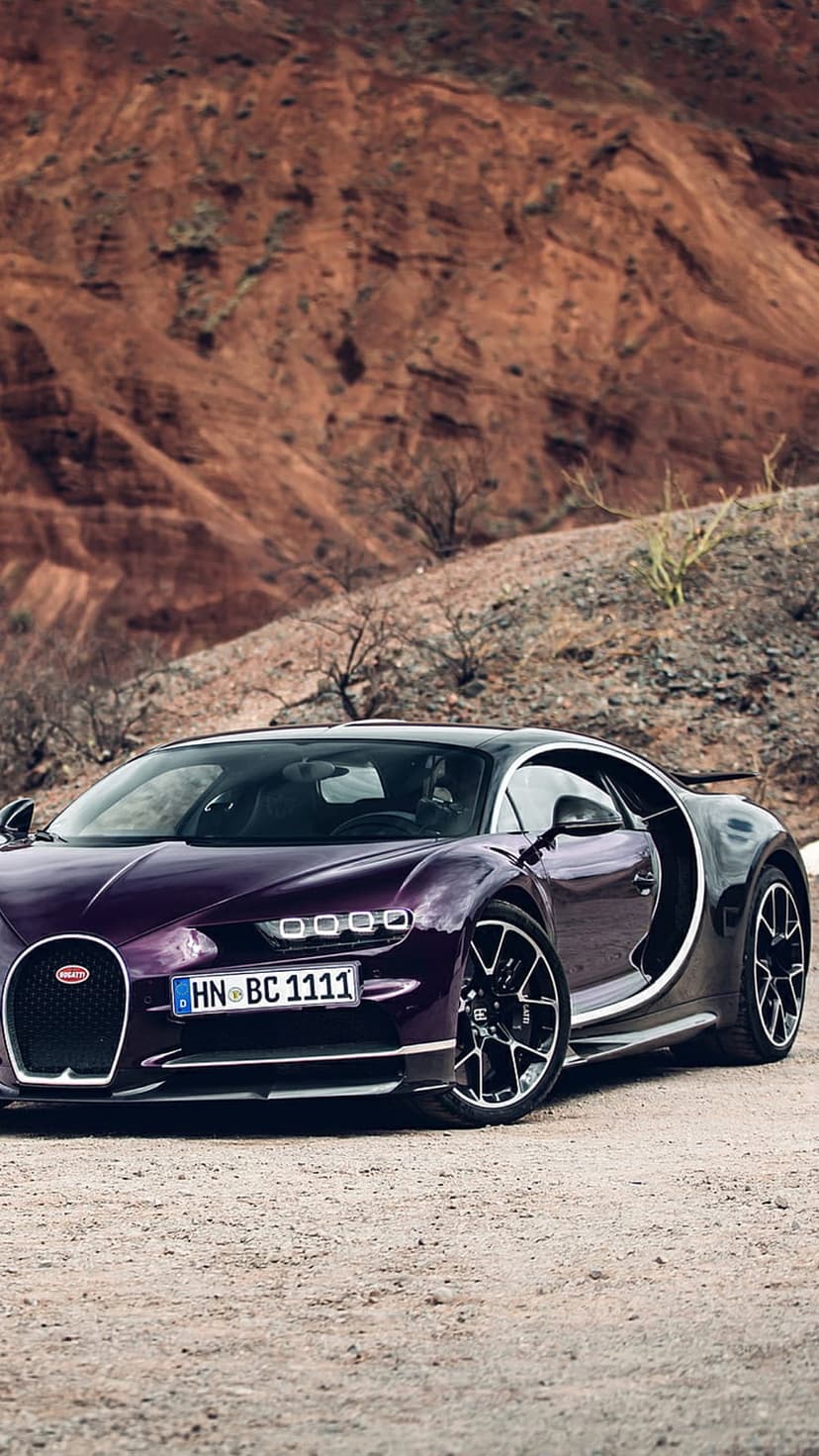 Purple Bugatti Chiron hypercar parked on a dry desert road with rocky mountains and sand in the background.