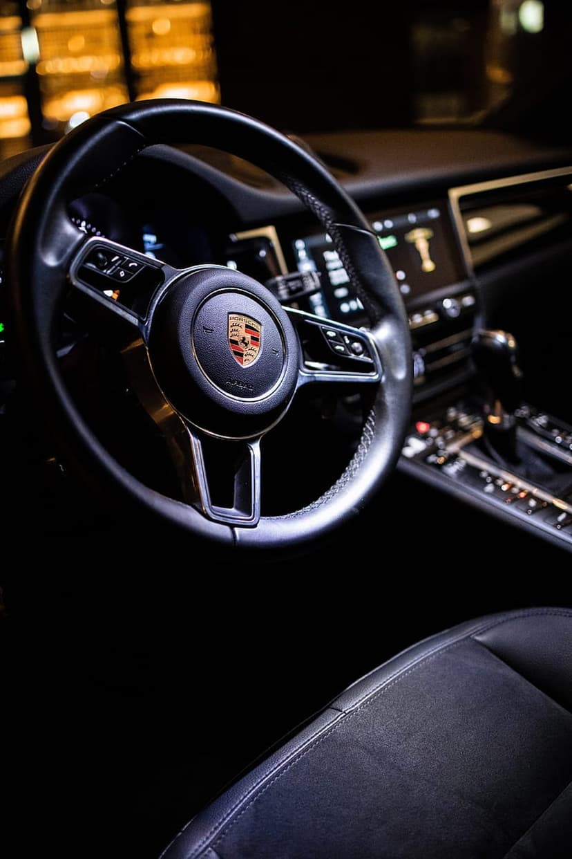 Porsche steering wheel with gold crest and leather textures next to a glowing infotainment system dashboard.