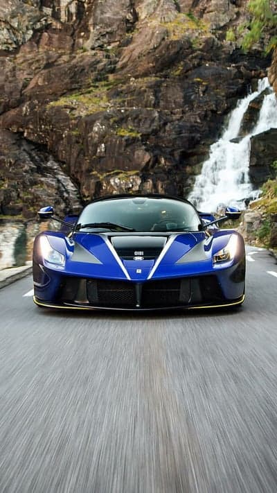 Blue Ferrari Drives Past Waterfall on Scenic Mountain Road
