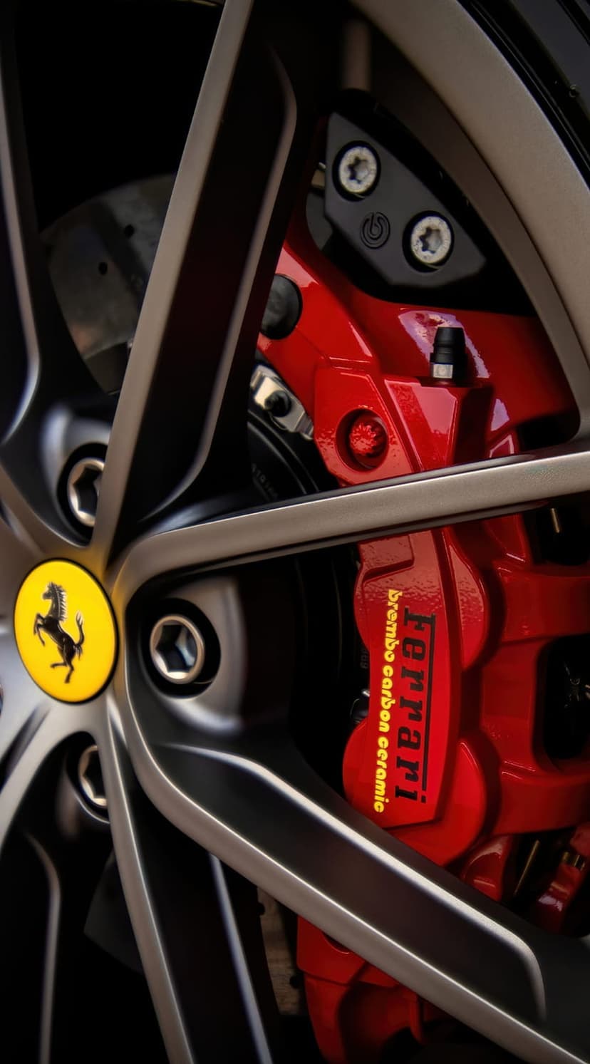 Red Ferrari brake caliper and yellow prancing horse emblem on a carbon ceramic wheel for mobile background use.