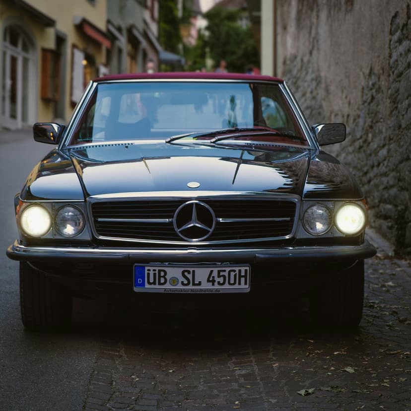 Black Mercedes-Benz SL 450 convertible with a burgundy top parked on a cobblestone European street at night.